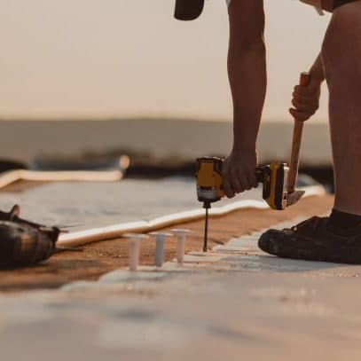 Roofer installing a flat roof membrane at dusk