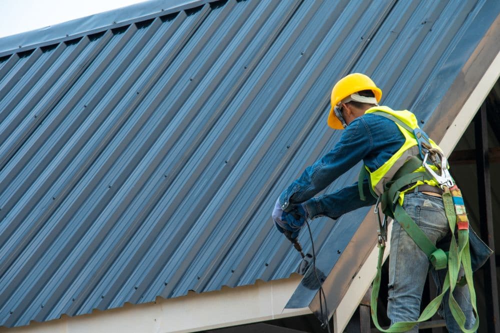 Roofer in a safety harness installing metal roofing panels