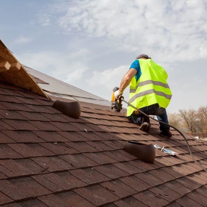 Roofer installing asphalt shingles with a nail gun