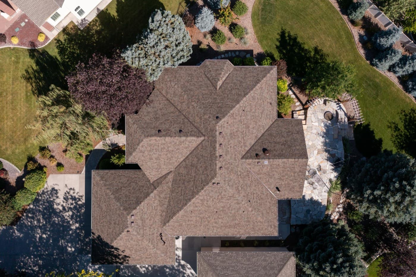 Aerial view of a large asphalt shingle roof surrounded by landscaped yard and trees